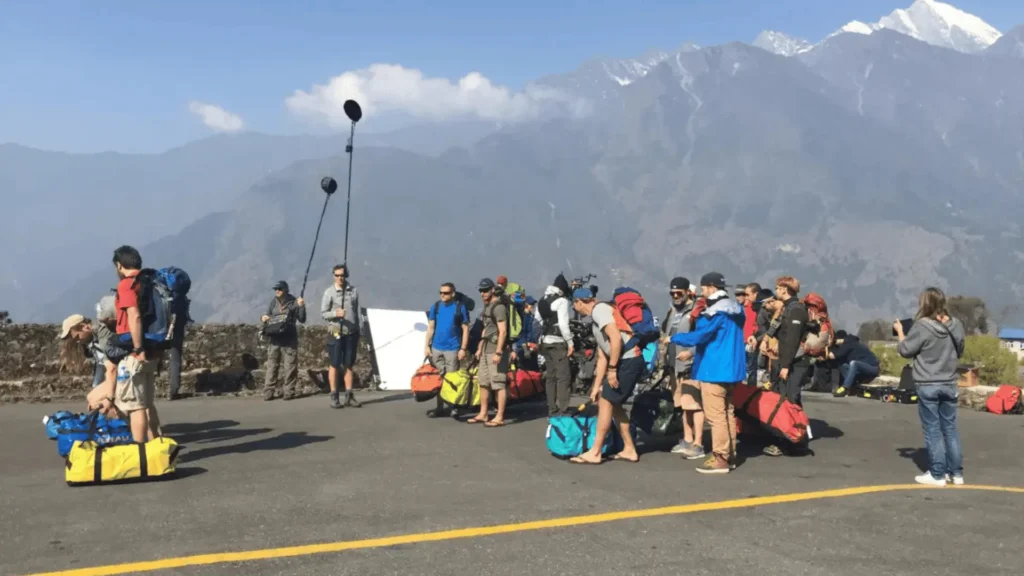 Large film crew assembling with equipment bags and boom microphone at a Himalayan airstrip as part of production planning in Nepal