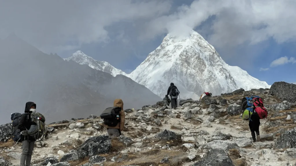 Film crew trekking with heavy backpacks toward a snow-capped Himalayan peak representing the challenges of filming logistics in Nepal