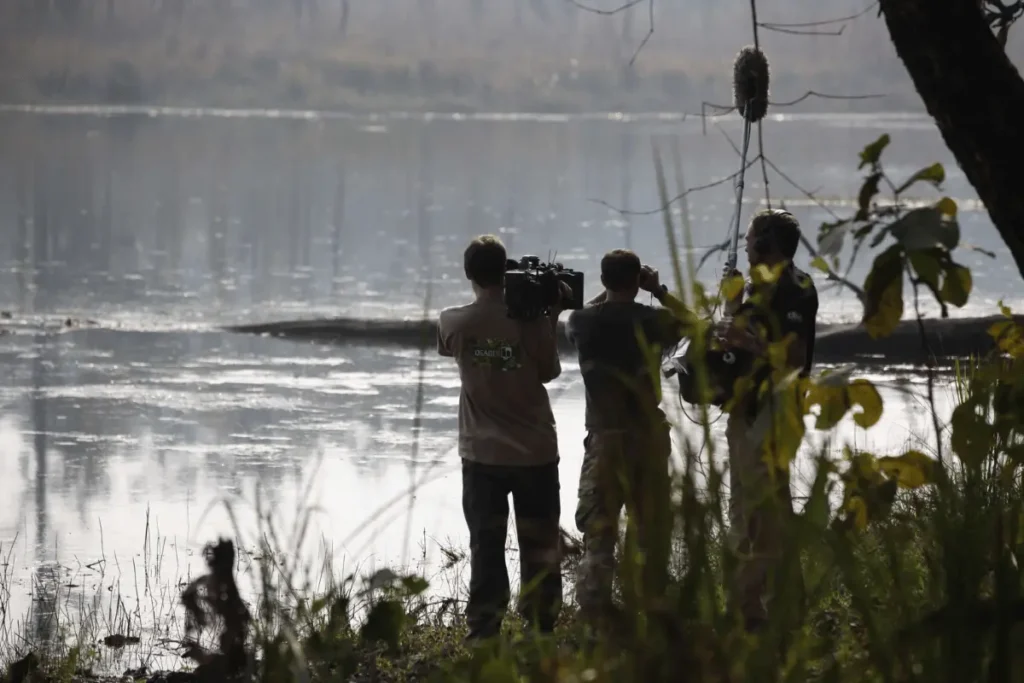 How to Film in Nepal Successfully: Ultimate Guide for International Productions (2026) Film crew with professional camera and boom microphone shooting by a mistry reflective lake surrounded by lush vegetarian while filming in nepal