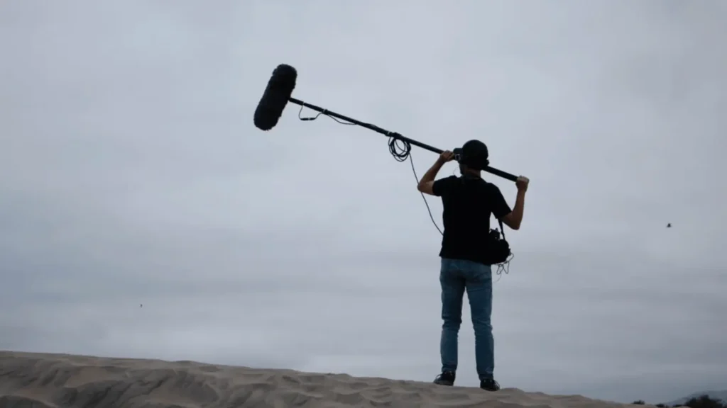 Boom operator recording location sound with a windshielded mic on a ridge.